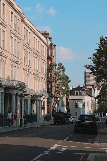 A wide street scene in Belsize Park showing a row of white Victorian-style residential buildings with decorative architectural features on the left, and a large tree with dense green foliage on the ri